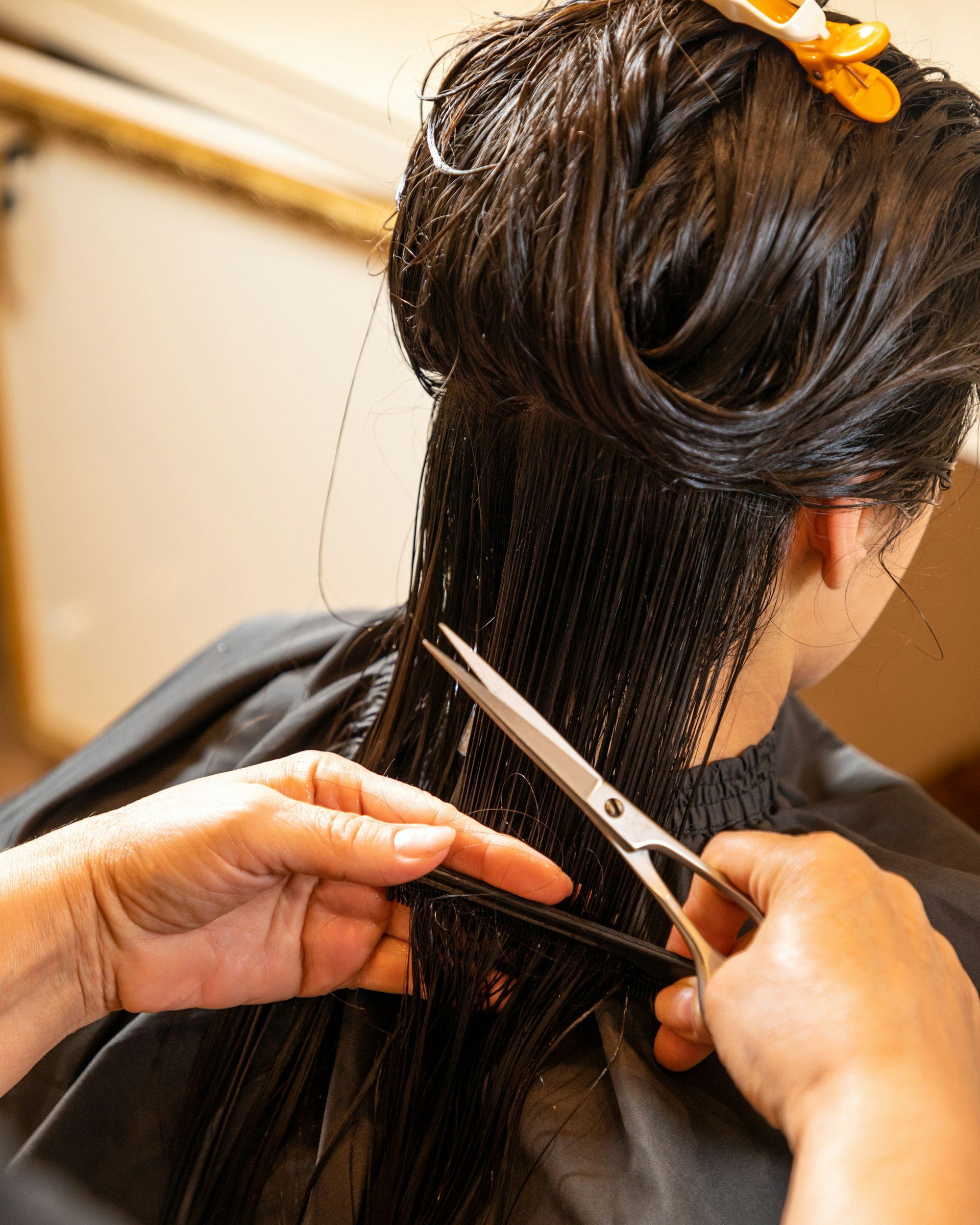 Scissors and a comb cutting a section of long, wet dark hair