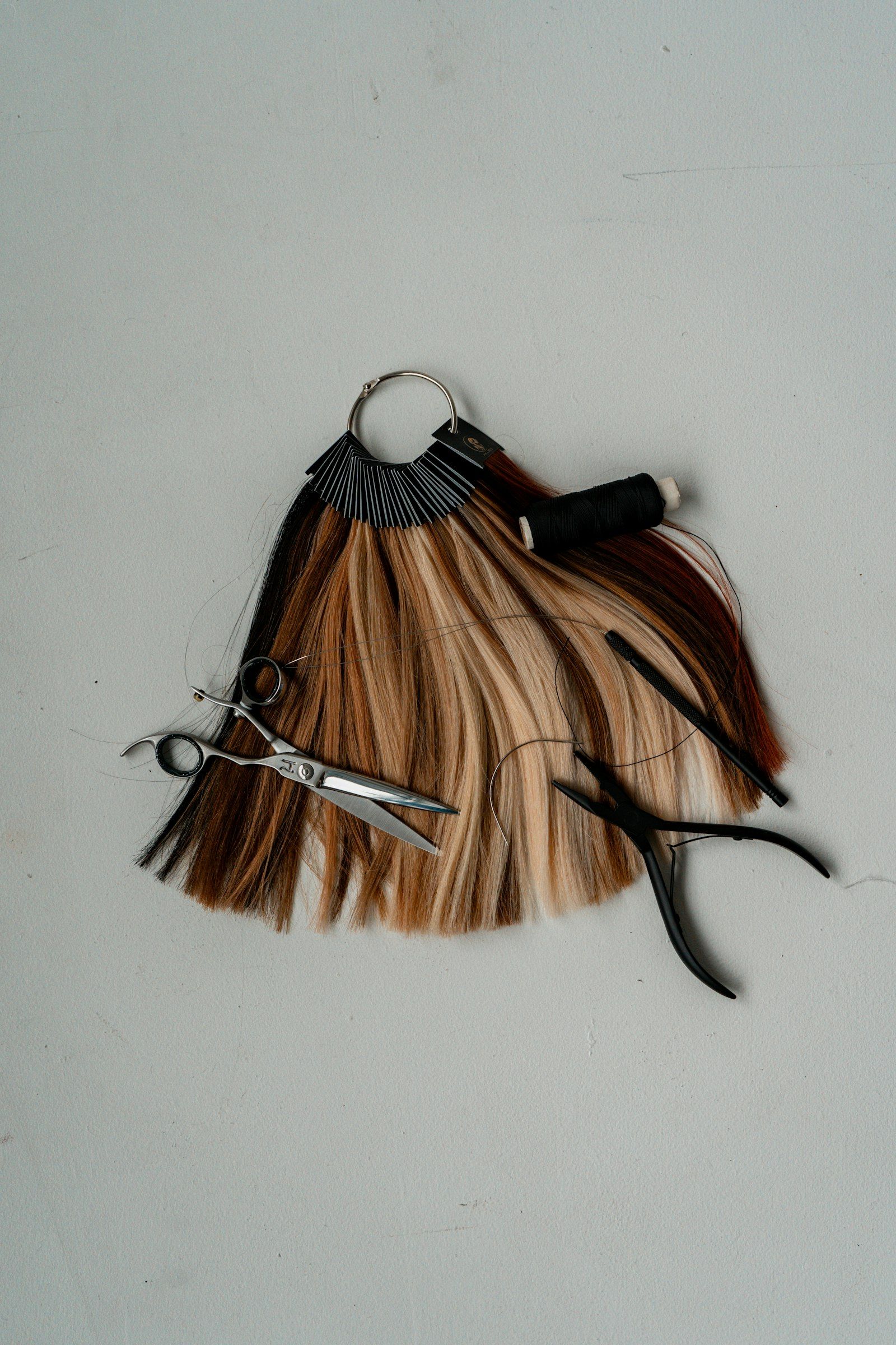 A colorist’s swatch ring of hair samples, from black through copper to pale blonde, beside shears