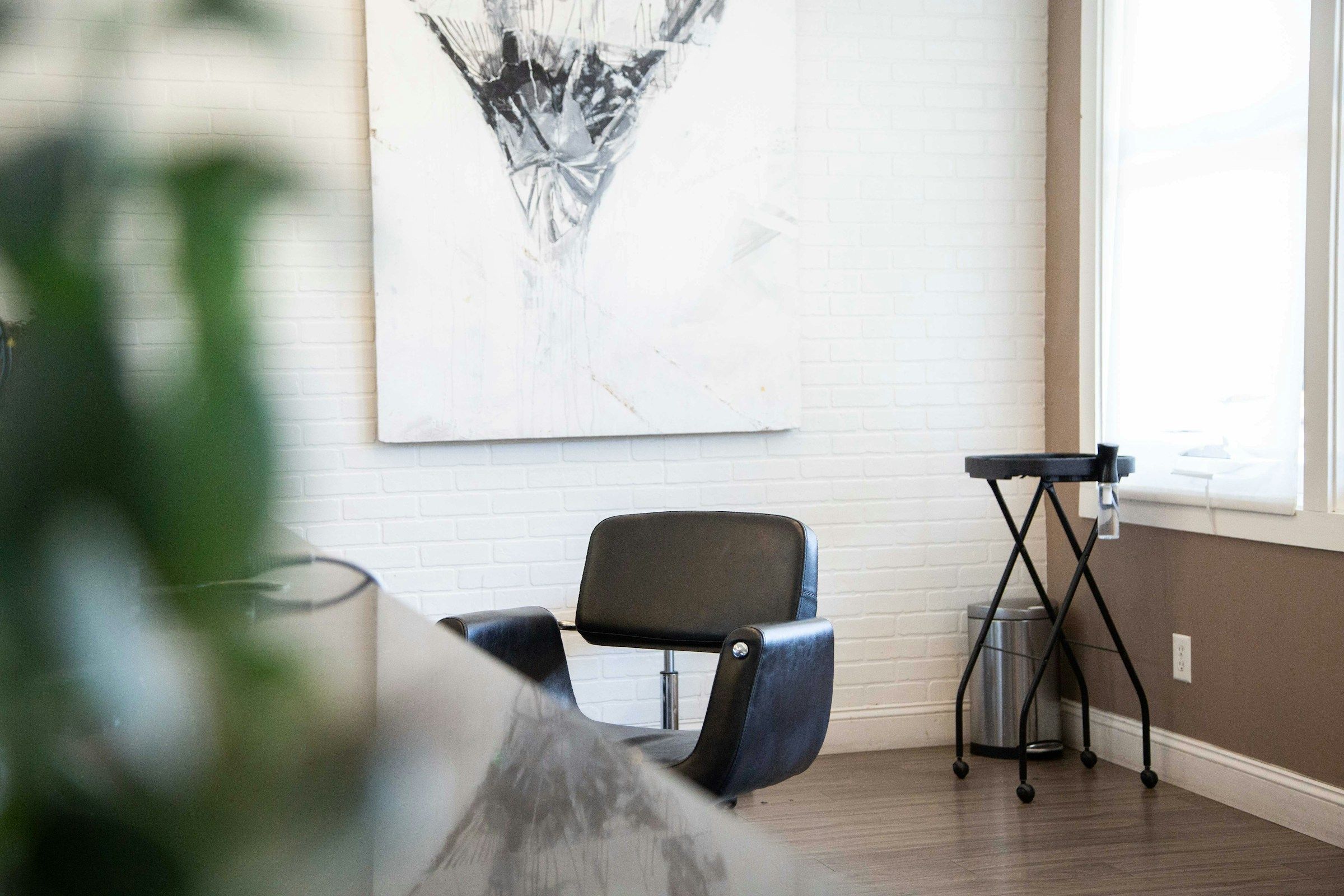 An empty black styling chair against a white brick wall, lit by a bright window