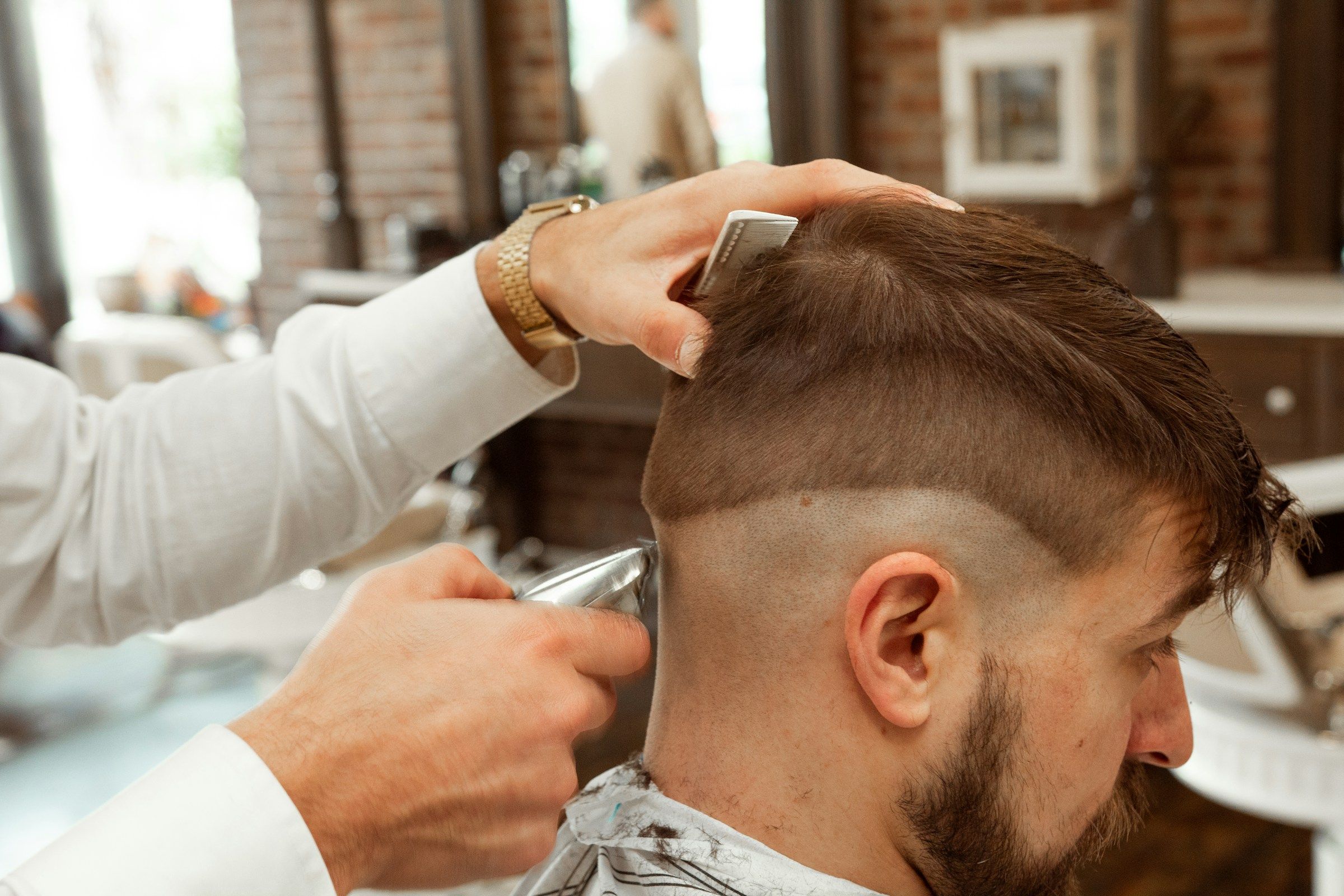 A barber using clippers and a comb on a short men’s cut